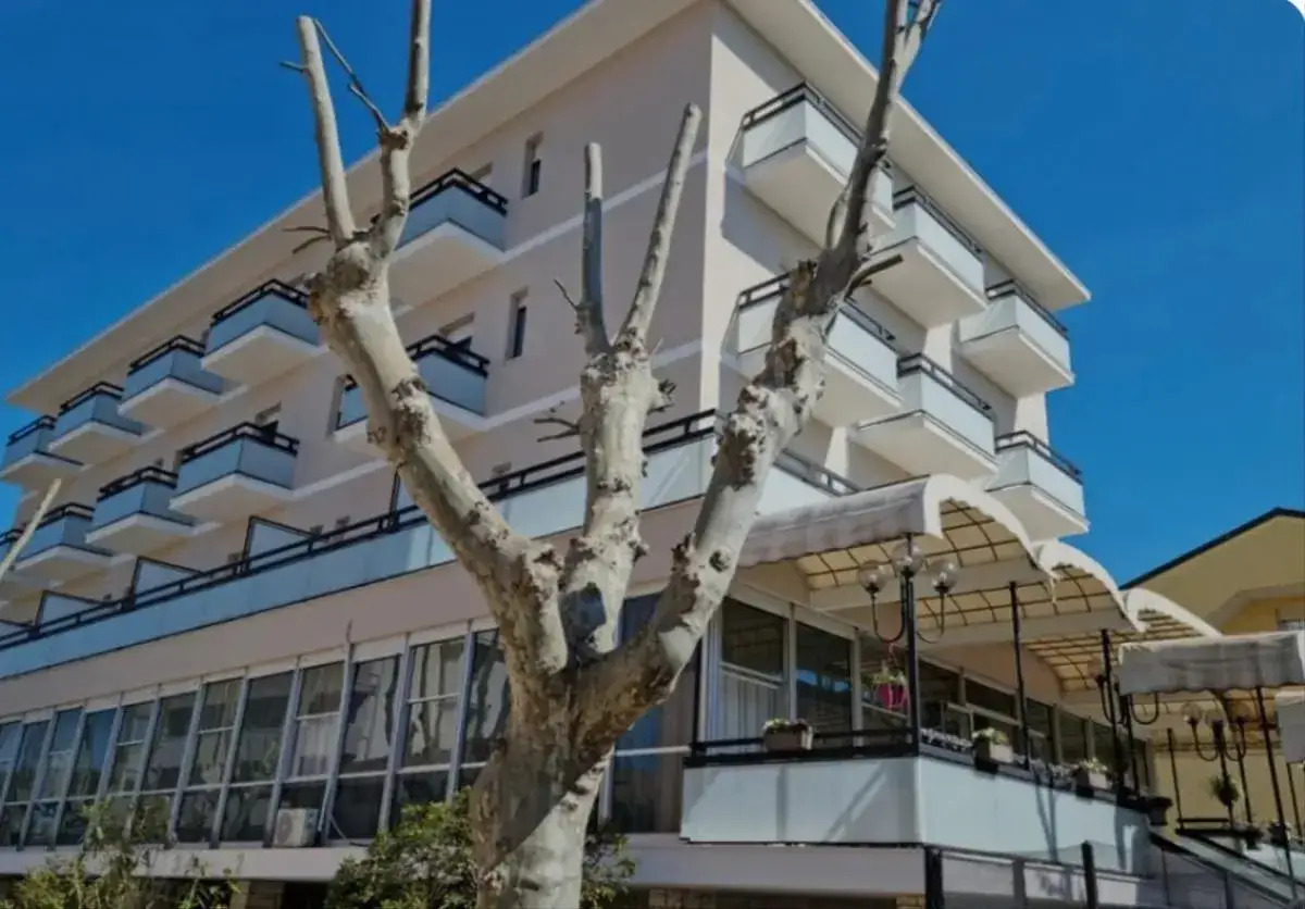 Edificio moderno con balconi e vetrate, un grande albero spoglio in primo piano. Il Kursaal Bellaria attende i suoi ospiti sotto un cielo azzurro.