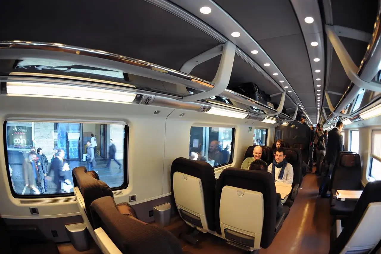 Interno di un Frecciarossa con passeggeri e bagagli ingombranti sui ripiani superiori.