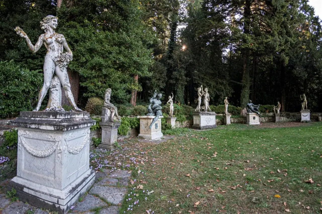 Sculture classiche adornano il giardino della Villa d'Ayala, tra alberi secolari e un prato fiorito.