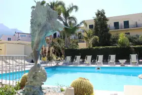 Scultura di pesce e piscina invitante al **hotel Punta del Sole Ischia**, circondata da palme e lettini.