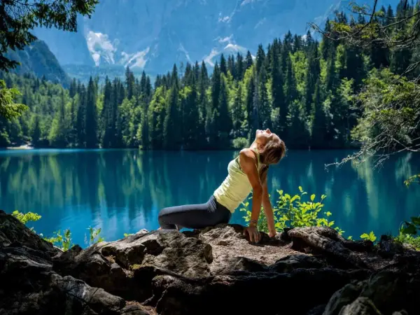 Donna in posa yoga su rocce, con lago turchese e montagne sullo sfondo. Un'immagine di serenità nella friuli montagna estate.