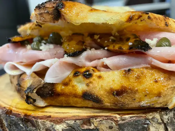 Un panino gourmet con mortadella, capperi e pomodori secchi, un vero re artù a Lecce, servito su un tagliere di legno.