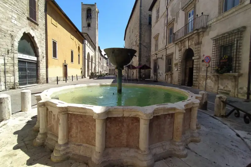 Fontana storica in pietra, un luogo incantevole tra le cose da vedere a Narni, con edifici antichi e un campanile sullo sfondo.
