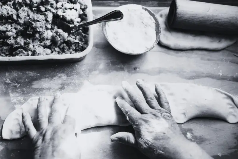 Mani esperte modellano la pasta per creare un'azdora romagnola, con ripieno e farina pronti.